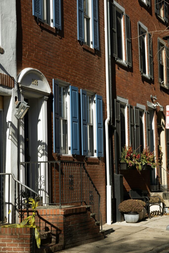 Brick townhouse with blue shutters, an arched white doorway and potted fall mums on the stoop