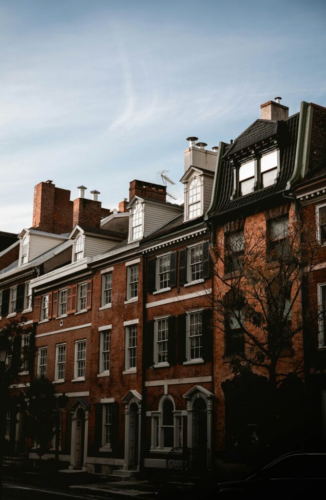 Row of historic red brick rowhouses with dormer windows and chimneys under a blue sky