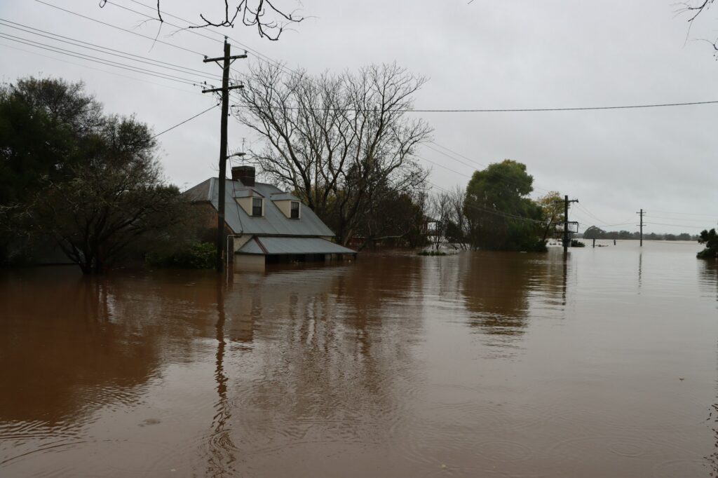 House with brown river floodwater up to its porch and bare trees on a gray day