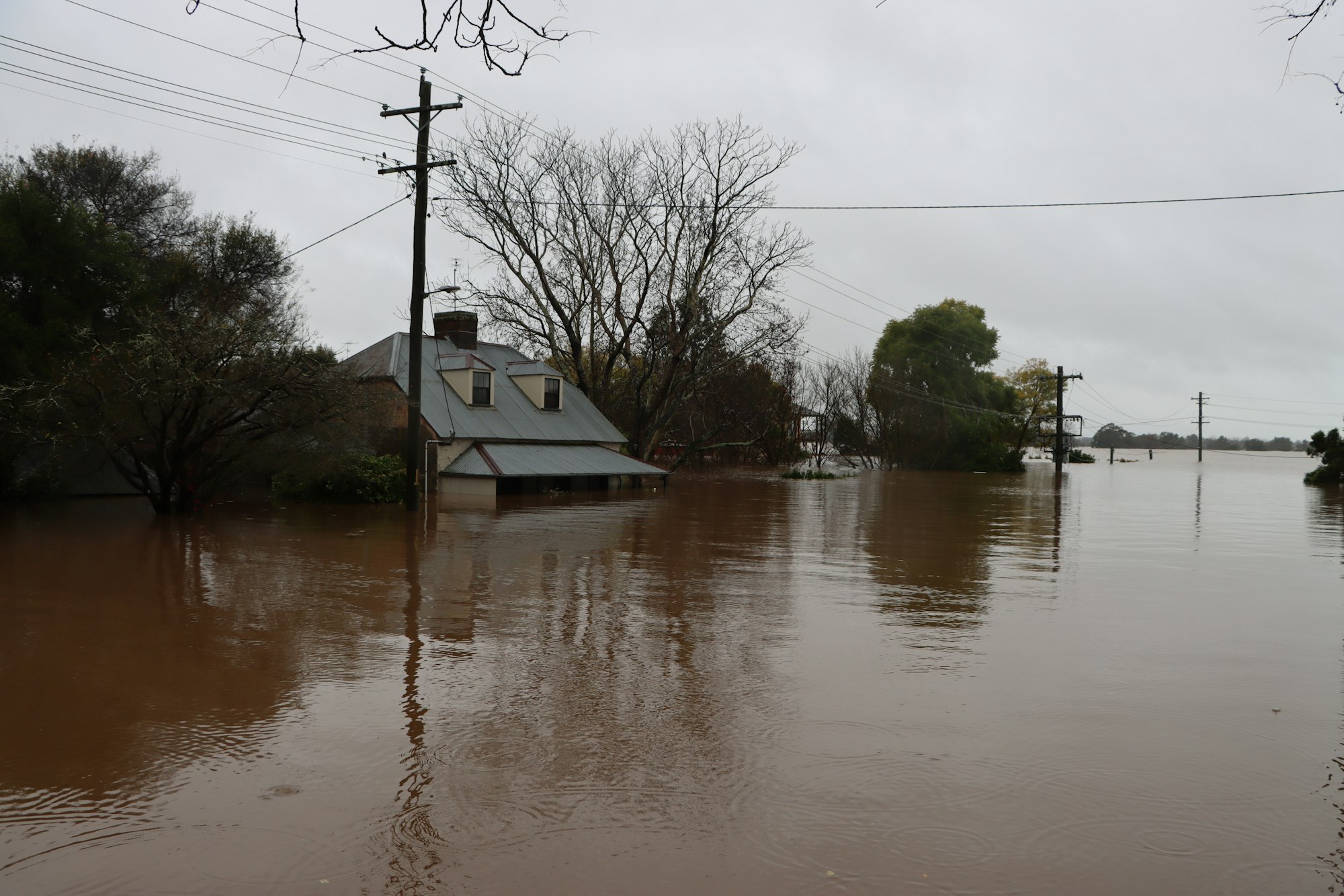 River floodwater around a house (Unsplash, Wes Warren) House with brown river floodwater up to its porch and bare trees on a gray day