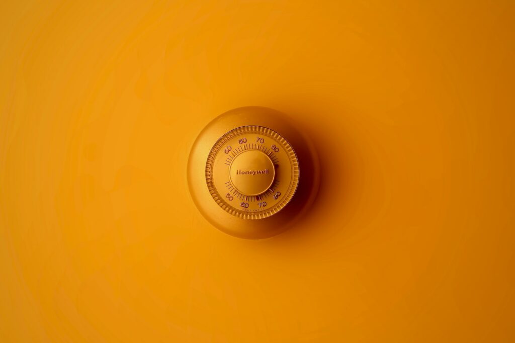 Round Honeywell dial thermostat mounted on a yellow painted wall