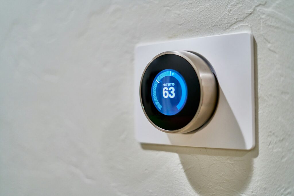 Round smart thermostat on a white textured wall showing a heat setting of 63 degrees